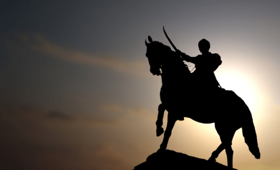 A swordsman on a horse atop a hill in silhouetter