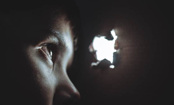 A frightened child looks through a small hole poked through a paper bag